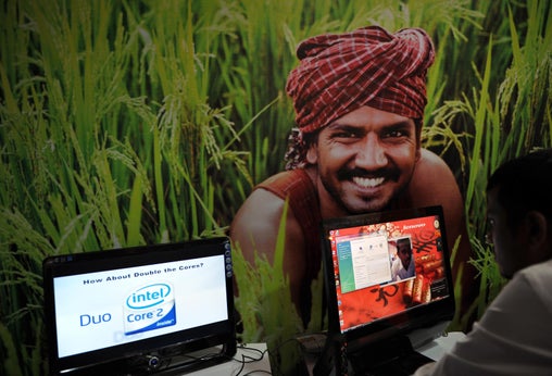 At an IT event in Karnataka, India, an attendee works on a computer in front of a poster of a farmer.